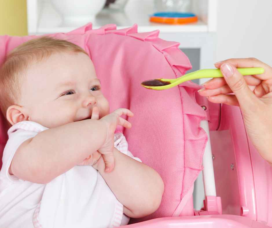Mom preparing homemade baby food with fresh fruits and vegetables in the kitchen while holding her baby