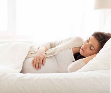 Pregnant woman sleeping on her left side with a pregnancy pillow—demonstrating safe and comfortable pregnancy sleep positions