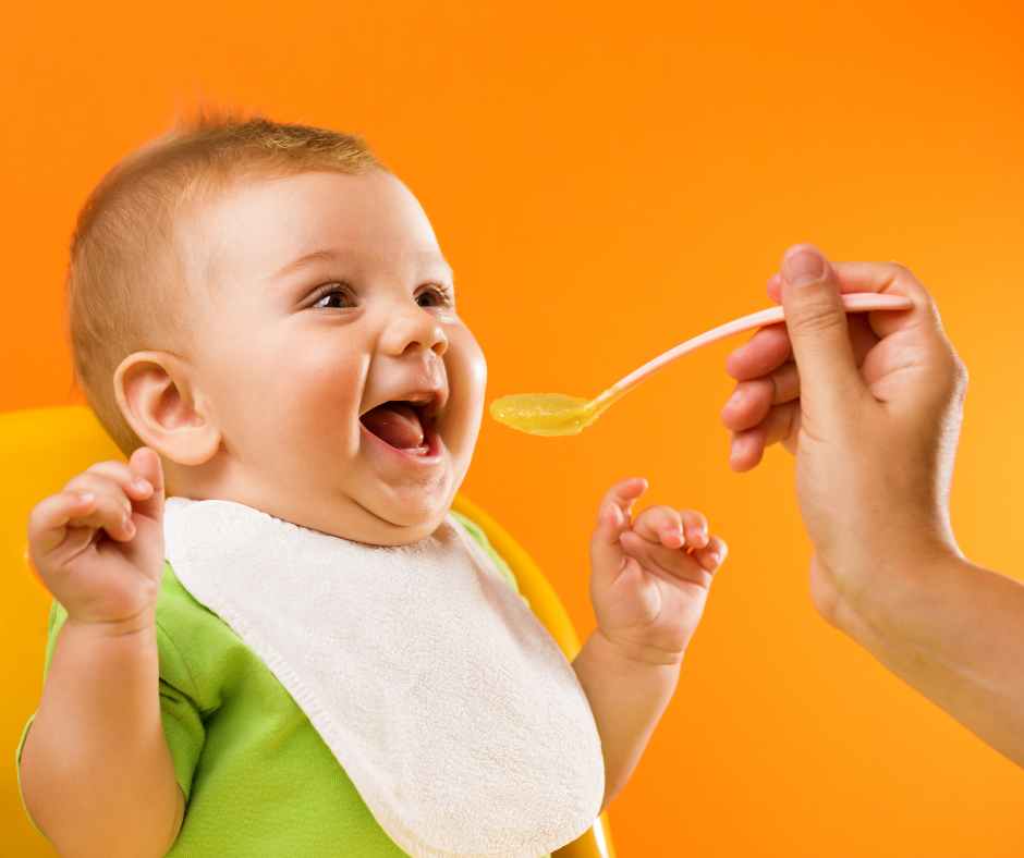 Starting solids for babies with mashed avocado served by mom using a spoon in a highchair
