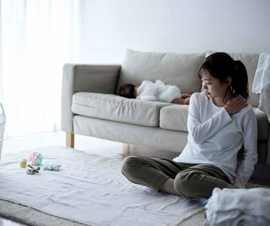 A tired mom sitting on the couch using a journal and essential oils from her self-care toolbox.
