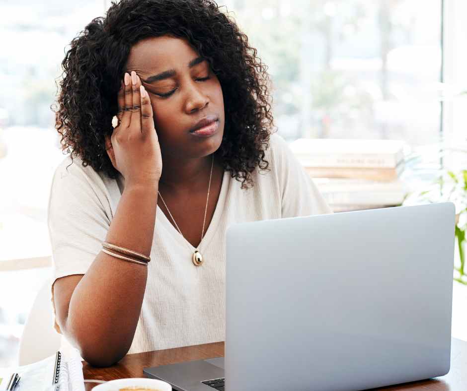 A tired mom sitting on the couch with her head in her hands, taking a quiet moment for self-care and burnout recovery.