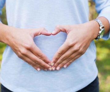 Pregnant woman sitting at a kitchen table with crackers, fruit, and tea—navigating first trimester nutrition despite nausea.