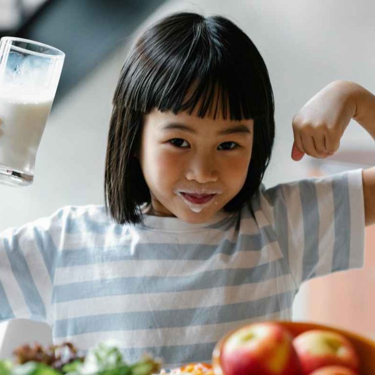 Toddler sitting at a table with three cups labeled milk, water, and juice—learning Healthy Beverage For Your Child.