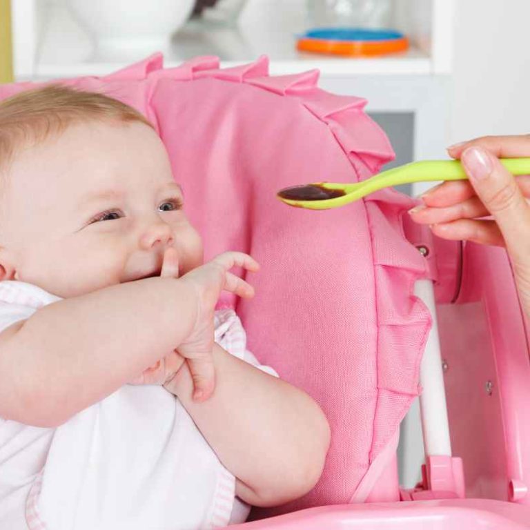 Mom preparing homemade baby food with fresh fruits and vegetables in the kitchen while holding her baby