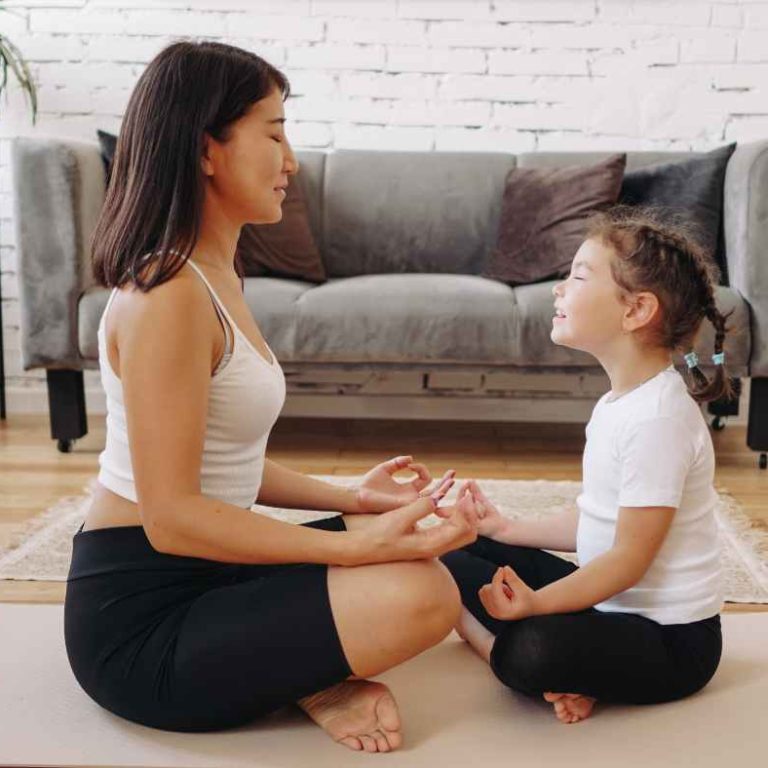 A mom sitting calmly with her child on the floor, smiling and making eye contact during a mindful parenting moment.