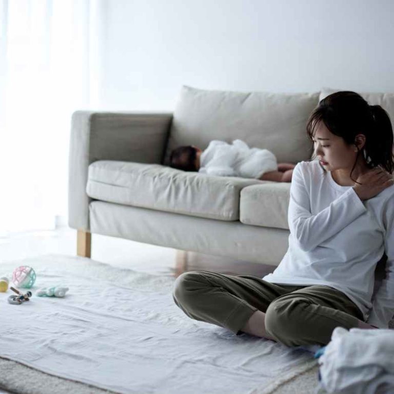 A tired mom sitting on the couch using a journal and essential oils from her self-care toolbox.